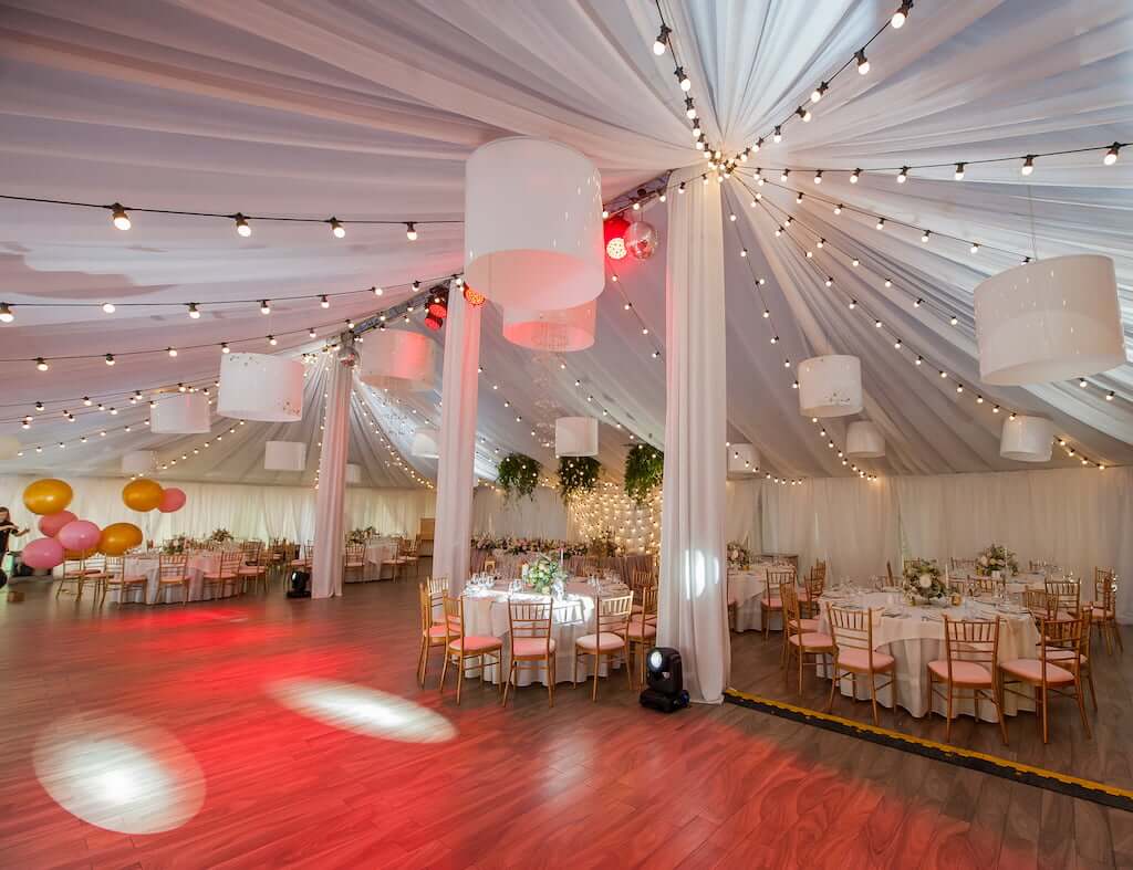 A wedding reception in a tent with tables and balloons, featuring talented ME DJs.