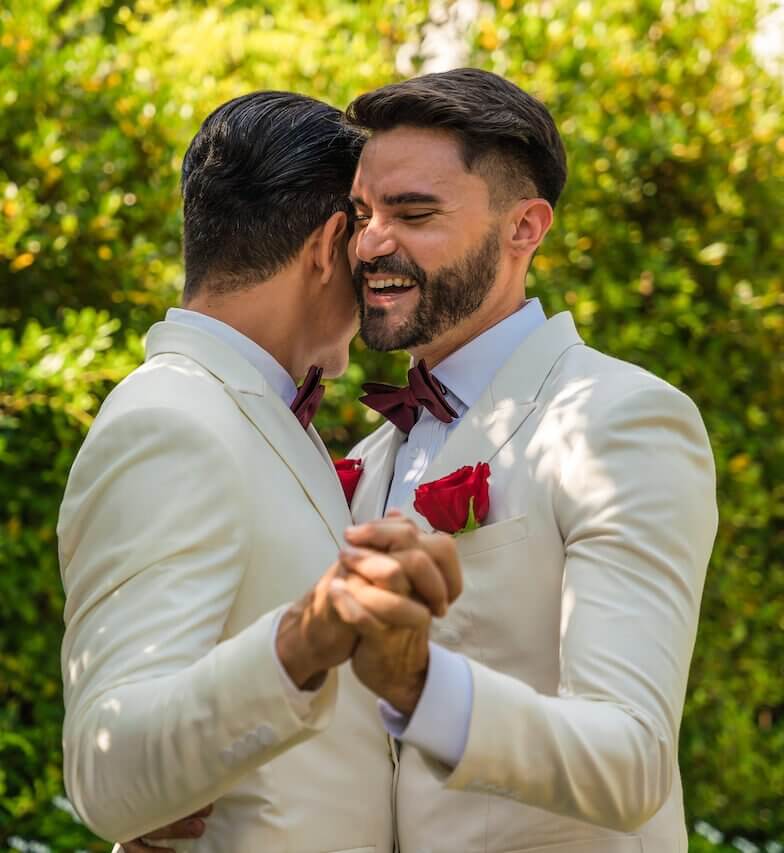 Two men in white tuxedos, hired as wedding DJs in Maine, dancing in the garden.