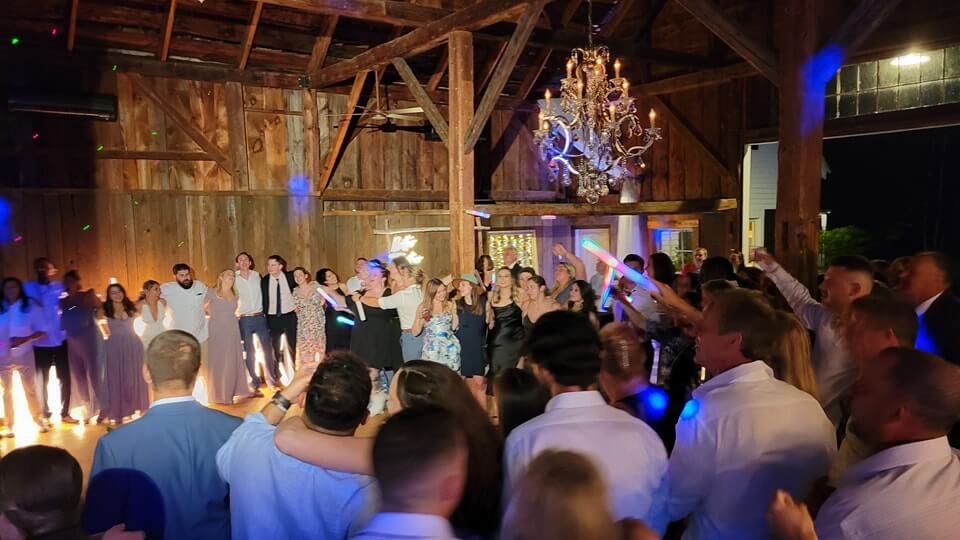 At one of the rustic barn wedding venues in New England, a lively group of people is joyfully dancing.