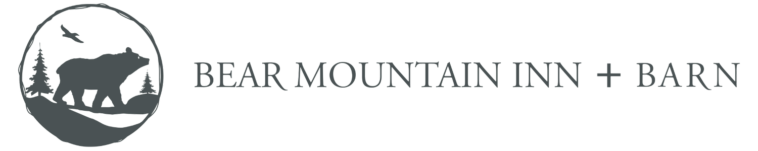 Logo for Bear Mountain Inn + Barn featuring a bear silhouette, trees, and a bird in a circular frame, with the business name in uppercase letters to the right.